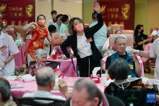 5月24日,在香港松悦园耆和护养院,安老事务委员会委员、香港乐龄社企“软餐侠”创办人文慧妍(中,穿黑色外套)带领职员扮演成“茶楼”经理、厨师和接待员,为老人家提供沉浸式茶楼就餐体验。新华社发(王申 摄)
