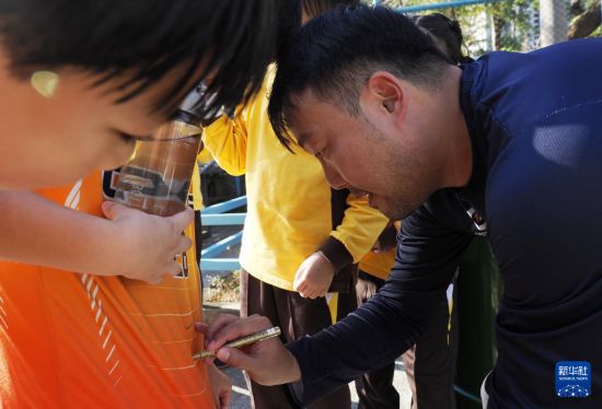 在香港新蒲岗彩虹道150号的露天游乐场，香港男子手球队主教练许文邦（右）在给小学生签名（2025年12月17日摄）。新华社发（王申摄）